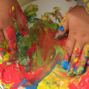 Mains d'un enfant jouant avec de la peinture multicolore, symbolisant la créativité et l'apprentissage par l'art